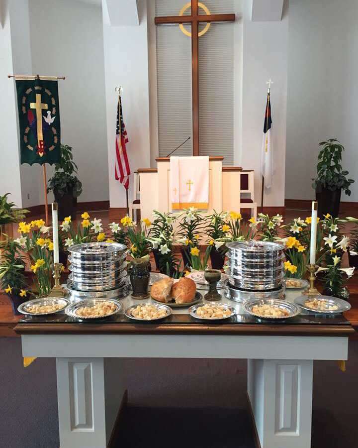 Communion table prepared for Easter Sunday worship. On the table, candles are lit, and surrounding the table are Easter lilies and daffodils.